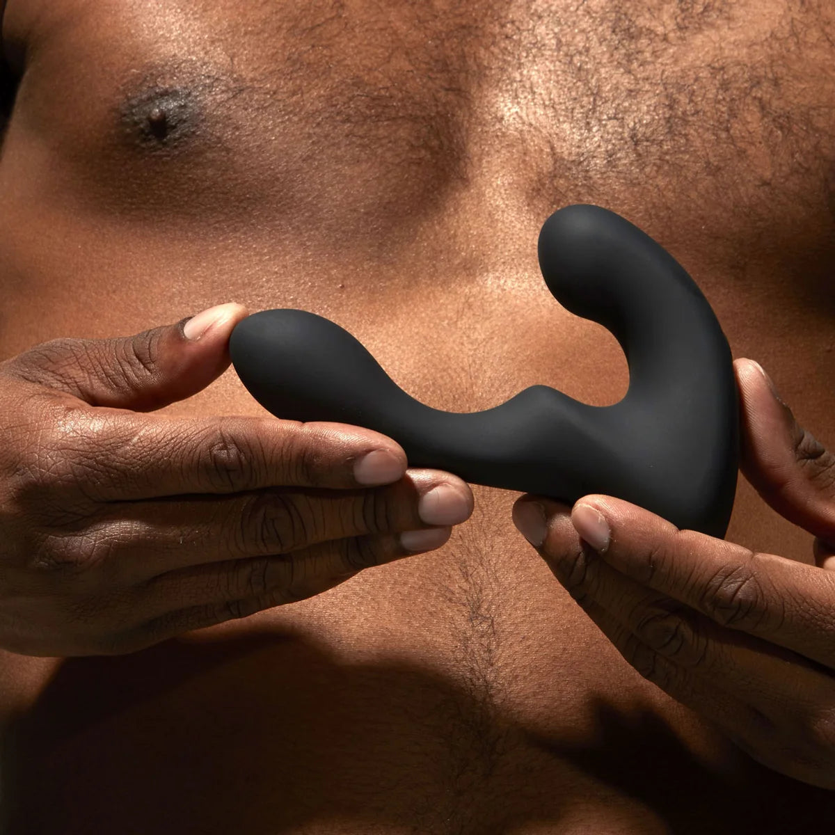 Black silicone butt plug held between two hands against a brown background